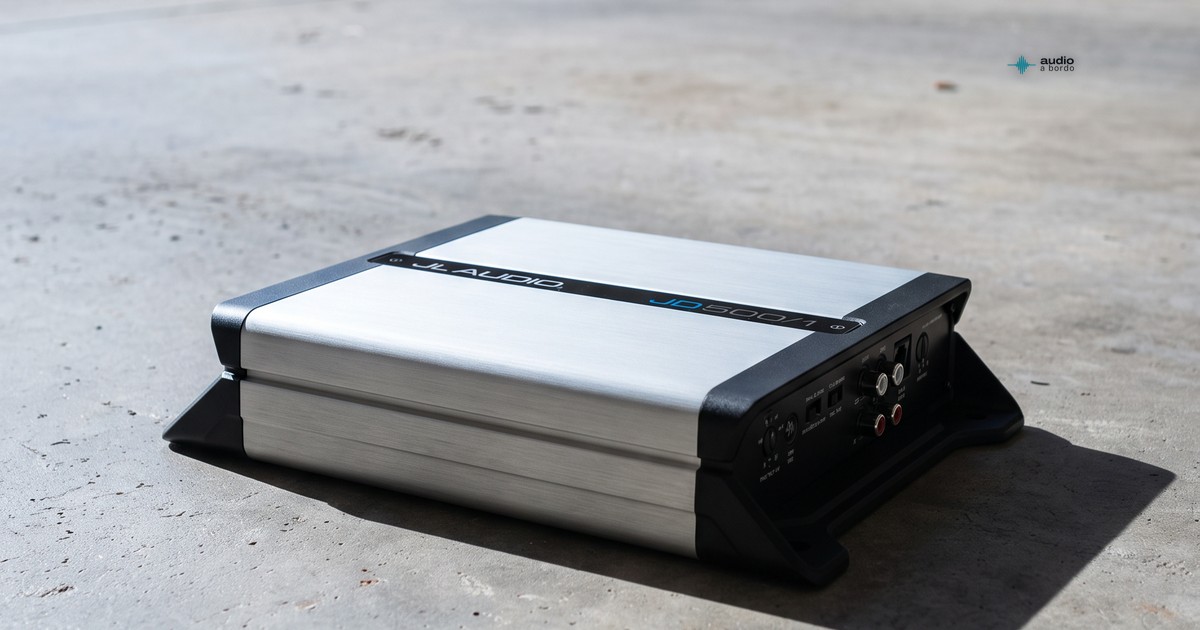Amplificador monoblock JL Audio JD500/1 de 500 W sobre concreto, con un auto desenfocado al fondo